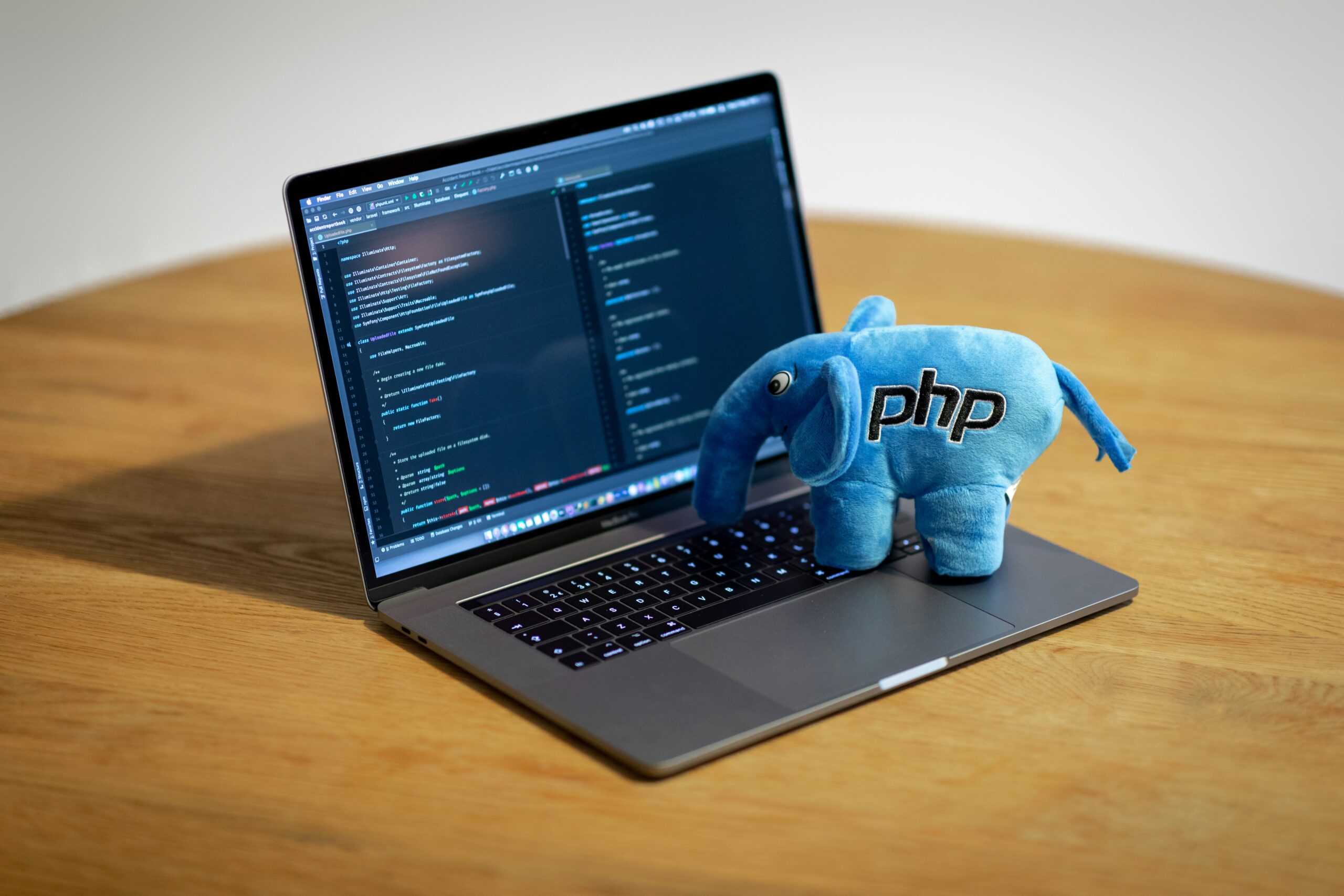 机の上に、開いたノートPCのキーボードの上に、PHPのアイコンの象のキャラクターの人形が乗っている